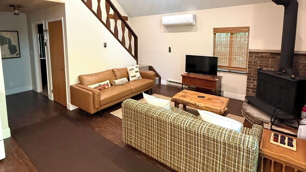 A living room with a brown sofa, a patterned ottoman, a wooden coffee table, a television, and a fireplace. - Golf • Fish • Hike • Located between Higgins & Houghton Lake (Roscommon)