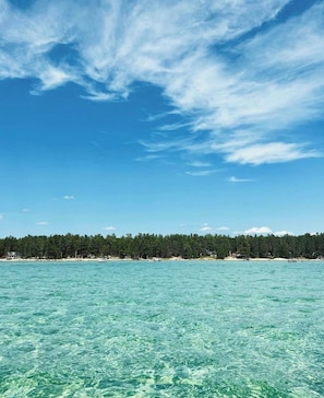A clear view of turquoise water, a forested shoreline, and a partly cloudy sky.