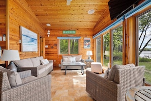 En inredning med trädetaljer och möbler i rotting, en skylt med texten ”STRANDHUS” och stora fönster.