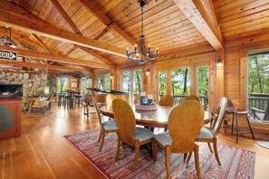 Un intérieur en bois agrémenté d’une cheminée en pierre, d’un lustre et d’un coin repas avec des chaises et une table.