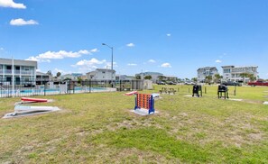 A grassy outdoor area with a pool, picnic tables, and a playground structure.