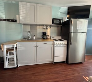 A kitchen with white cabinets, a stainless steel refrigerator, a microwave, a stove, and a wooden countertop.