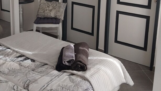 A bedroom with a bed, a chair, a table, and two doors. - A Casa bianca (Lozzi)