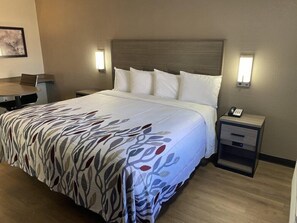 Quarto de hotel com uma cama, mesas de cabeceira, escrivaninha e uma cadeira.