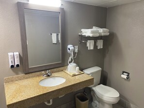 A bathroom with a granite countertop sink, a mirror, a hairdryer, a towel rack, and a toilet. - Red Roof Inn Jacksonville, AL (Jacksonville)