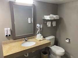 A bathroom with a granite countertop sink, a mirror, a hairdryer, a towel rack, and a toilet.