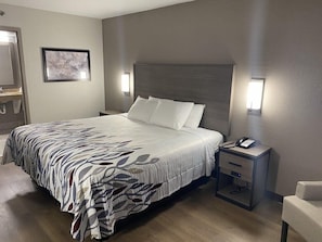 Quarto de hotel com cama, mesa de cabeceira e uma cadeira.