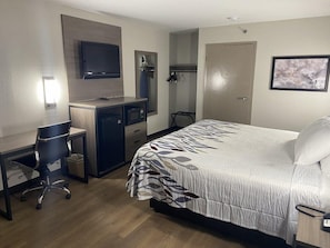 Quarto de hotel com cama, escrivaninha, cadeira, televisão e porta.