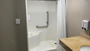 A bathroom with a shower, grab bar, and a sink with a soap dispenser.