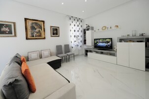 A modern living room with a sofa, chairs, a TV, and a white cabinet.
