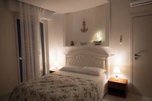A bedroom with a bed, nightstands, a wall-mounted shelf with decorative items, and a door.