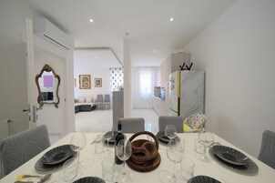 A dining area with a white table set for six, a bottle of wine, and a mirror on the wall.