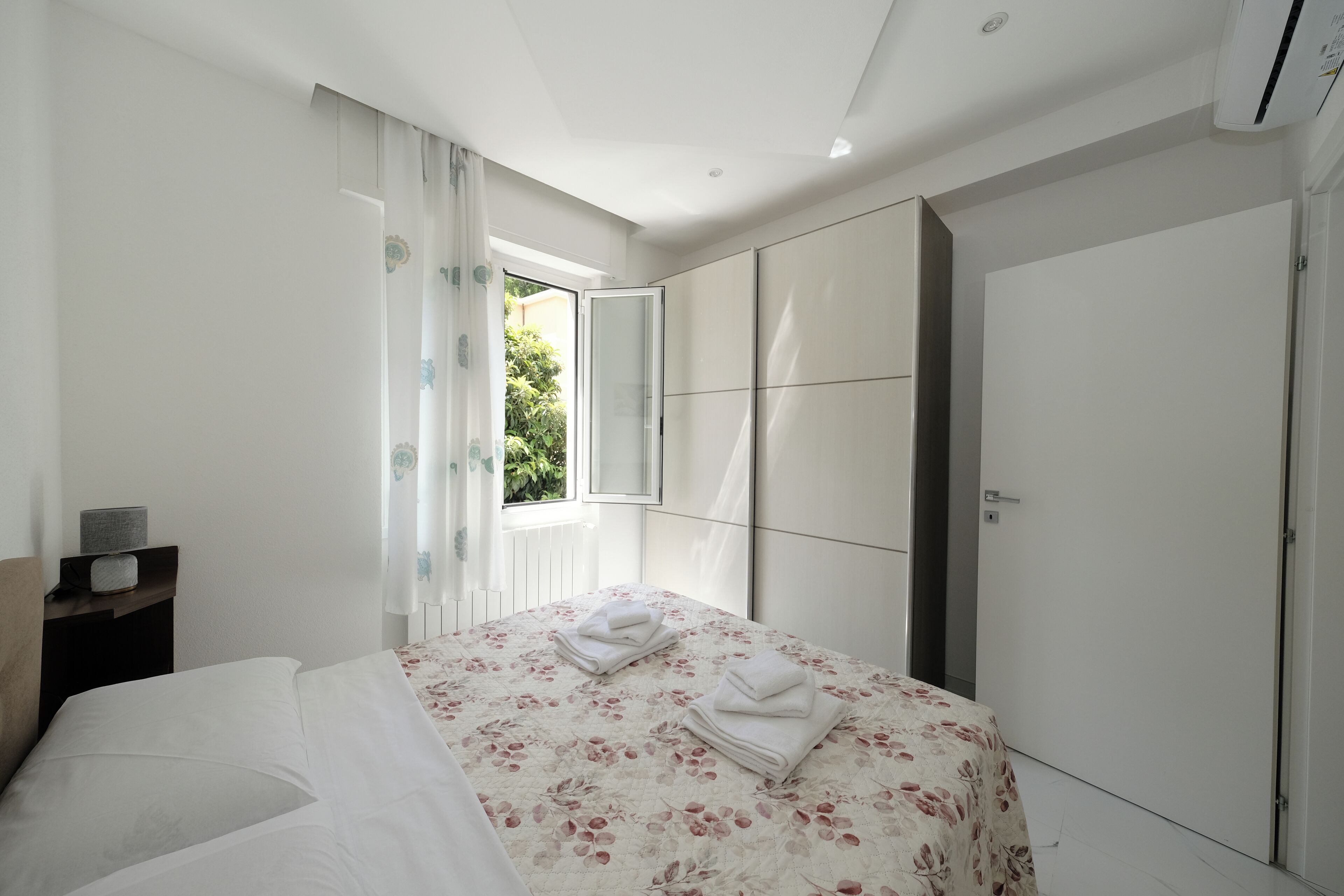 Ein Schlafzimmer mit Bett, Kleiderschrank, Fenster und Nachttisch.