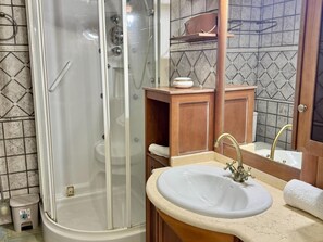 Een badkamer met een douchecabine van glas, een wastafel met een gouden kraan en een houten wastafelmeubel.