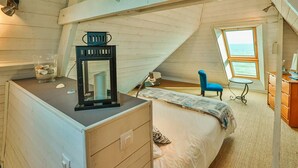 Un dormitorio con cama, cómoda, espejo, silla y ventana con vistas.