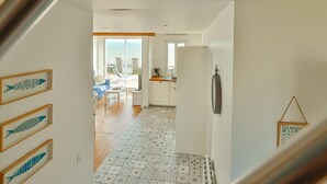 Una cocina moderna con refrigerador, un comedor con mesa y sillas, y vista al mar a través de un ventanal grande.