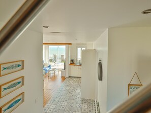 Une cuisine moderne équipée d’un réfrigérateur, un coin repas avec une table et des chaises, et une vue sur la mer grâce à une grande fenêtre.