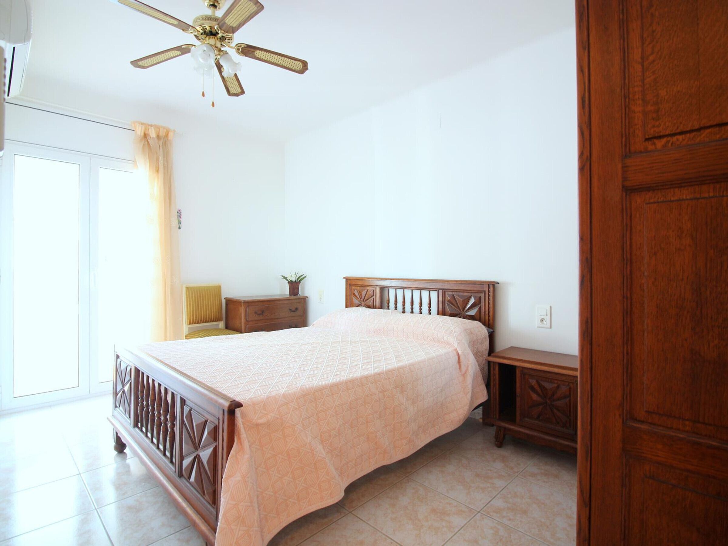 A bedroom with a bed, a nightstand, a dresser, a ceiling fan, and a door.