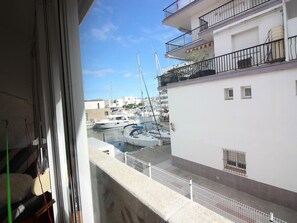 Blick auf eine Marina mit vertäuten Booten, ein weißes Gebäude mit Balkonen und einem klaren Himmel.