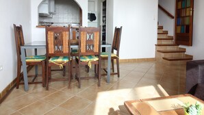 Een eetgedeelte met een tafel en stoelen, een keuken op de achtergrond, en een trap naar een ander niveau.