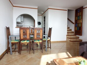 Ein Essbereich mit Tisch und Stühlen, im Hintergrund eine Küche und eine Treppe, die zu einer weiteren Ebene führt.