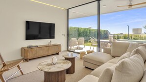 Ein modernes Wohnzimmer mit Fernseher, Holzmöbeln und Blick auf einen Pool und Grünflächen.