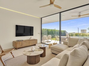Ein modernes Wohnzimmer mit Fernseher, Holzmöbeln und Blick auf einen Pool und Grünflächen.