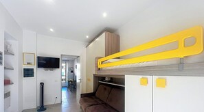 Habitació senzilla amb lliteres, televisió, petita cuina i zona de menjador.