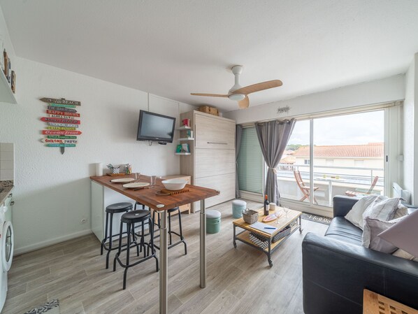A compact living space with a kitchenette, a dining area, a sofa, a TV, and a balcony with a view. - Cozy studio, beachfront location - 2 guests (Biscarrosse Plage)