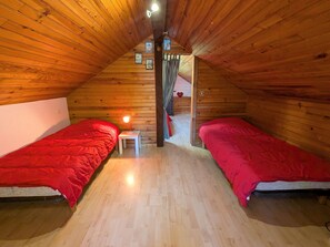 Une chambre confortable située sous les toits, avec deux lits simples, une petite table de chevet avec une lampe et un plafond en bois.