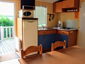 A compact kitchen with a refrigerator, microwave, sink, and stove. There are two wooden chairs and a table.
