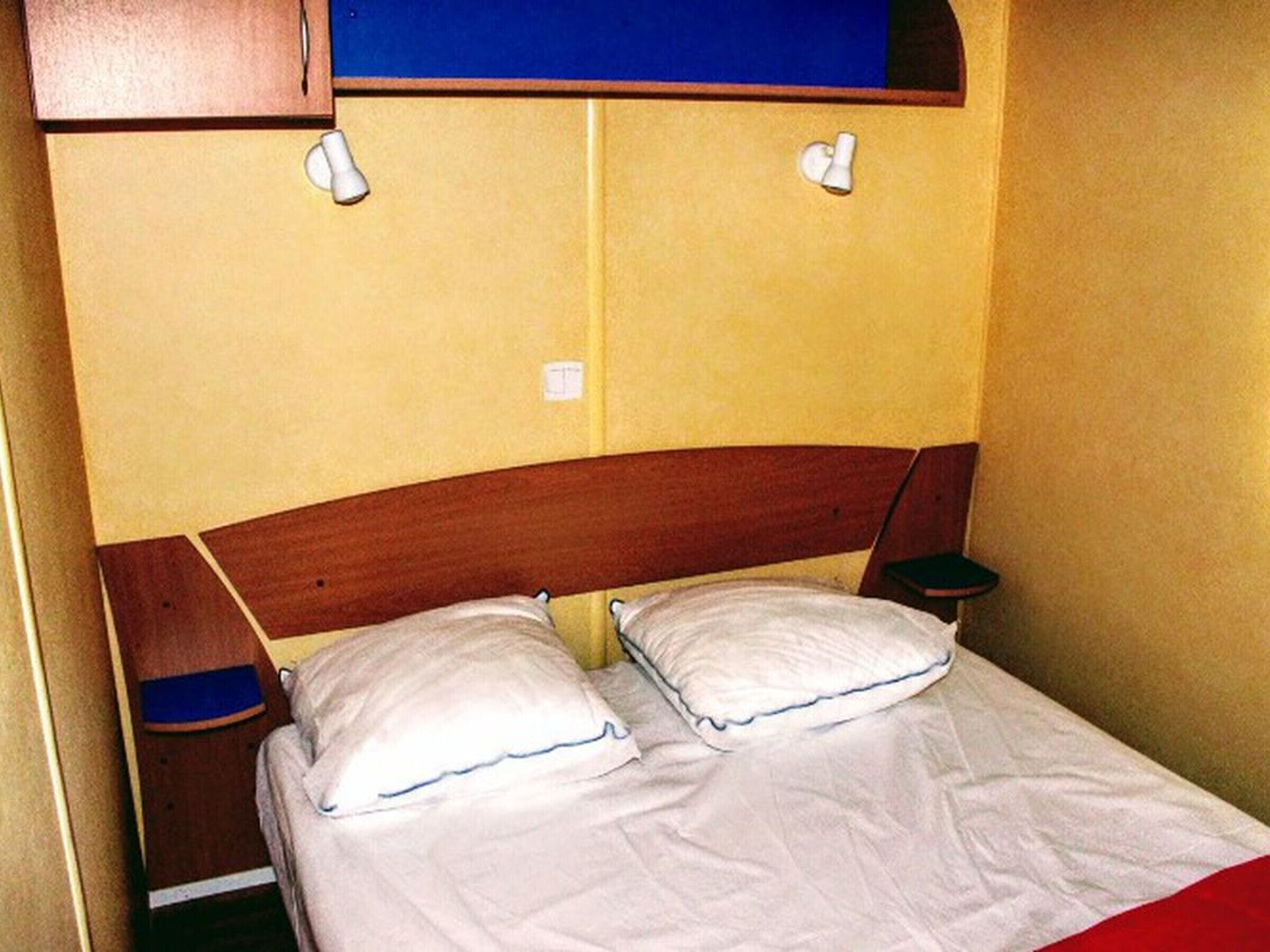Un lit simple avec une literie blanche et deux oreillers, une tête de lit en bois et une petite table de chevet.