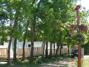 A row of mobile homes with wooden decks, surrounded by trees and a red sign. - Mobile home for 4 guests, pets allowed (Verteillac)