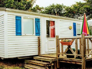 A mobile home with a wooden deck, a door, and a window with blue shutters. - Mobile home for 4 guests, pets allowed (Verteillac)