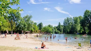 A lakeside beach with people swimming and relaxing, surrounded by trees.