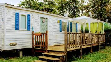 A mobile home with a wooden deck and steps leading to the entrance.