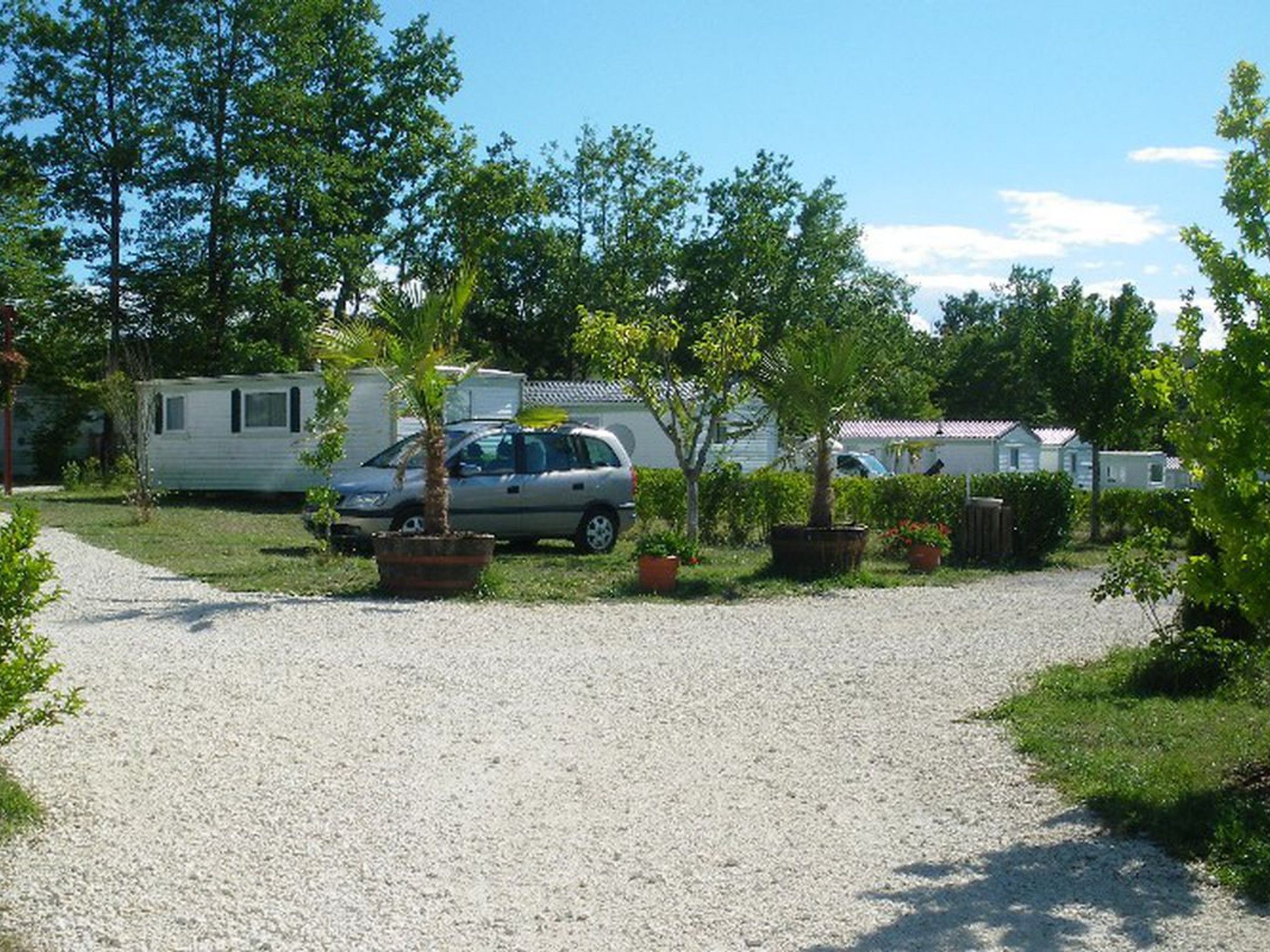 Un espace de stationnement recouvert de gravier, avec une voiture et une caravane.