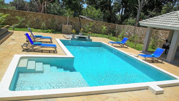Ein rechteckiger Pool mit einer Steinterrasse, umgeben von Liegestühlen und einer überdachten Sitzgruppe.