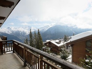 Ein hölzerner Balkon mit Blick auf schneebedeckte Berge und eine darunterliegende Stadt.