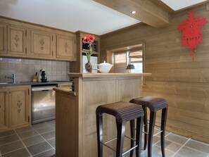 Eine Küche mit Holzausbau, einem Edelstahl-Geschirrspüler, einer Bar mit Hockern und einer roten Uhr an der Wand.