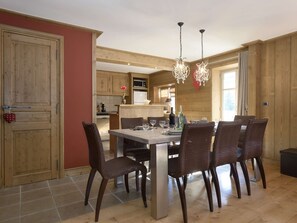 Ein Essbereich mit einem für sechs Personen gedeckten Tisch, umgeben von Korbstühlen, in einem Raum mit Holzwänden und einer Kristallleuchter.