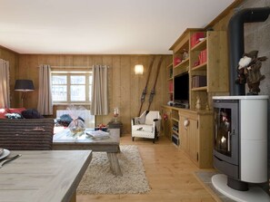 Ein gemütliches Wohnzimmer mit Holzvertäfelung, einem Kamin, einem Fernseher und einem Essbereich mit Tisch und Stühlen.
