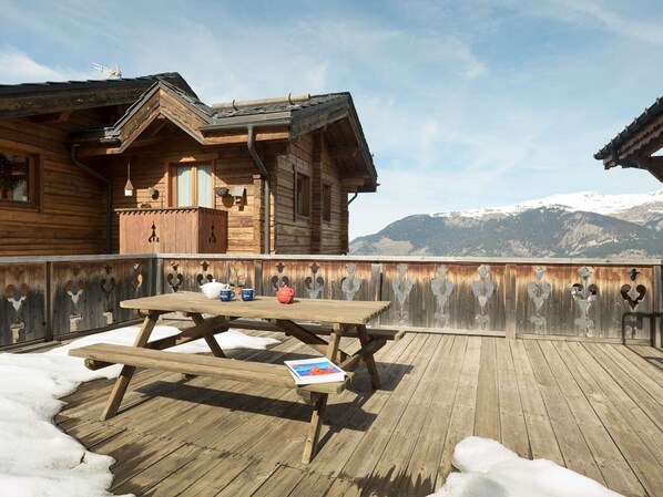 Eine Holzdar Terrasse mit Picknicktisch, eine Holzhütte mit geneigtem Dach und eine gebirgige Kulisse.