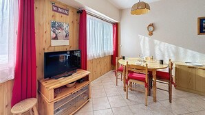 Ein gemütliches Zimmer mit einer Holz-TV-Kommode, einem Esstisch mit Stühlen, einem roten Vorhang und einem Rauchverbot-Schild.