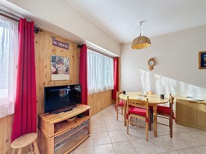 Ein gemütliches Zimmer mit einer Holz-TV-Kommode, einem Esstisch mit Stühlen, einem roten Vorhang und einem Rauchverbot-Schild.