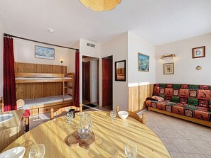 Ein gemütliches Zimmer mit einem Etagenbett, einem Holzessttisch, einer gemusterten Couch und einer kleinen Küchenzeile.