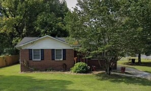 A single-story brick house with a front yard, a tree, and a small garden area. - Cozy 2-bedroom house in perfect College Park with AC (College Park)
