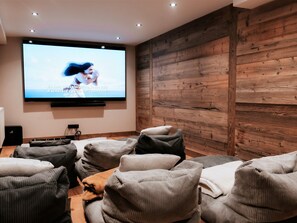 Ein moderner Heimkino-Raum mit einem großen Flachbildfernseher an der Wand, einer Holzpaneelausstattung und mehreren gepolsterten Sitzbereichen.