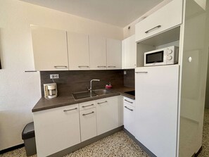 Una cocina compacta con armarios blancos, un lavamanos de acero inoxidable, un microondas y una cafetera.