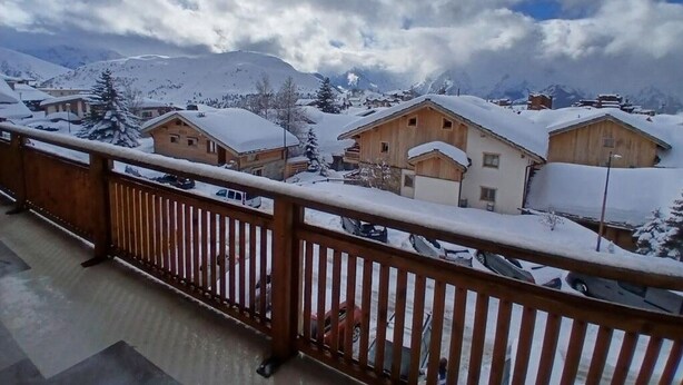 Un pueblo montañoso cubierto de nieve con casas de madera y un balcón con barandilla de madera.